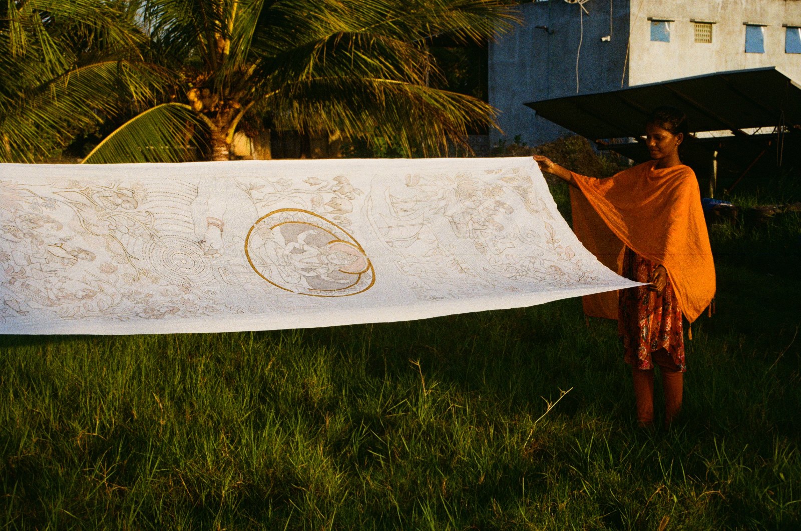 An artisan holding open a long painted kalamkari cloth in a field