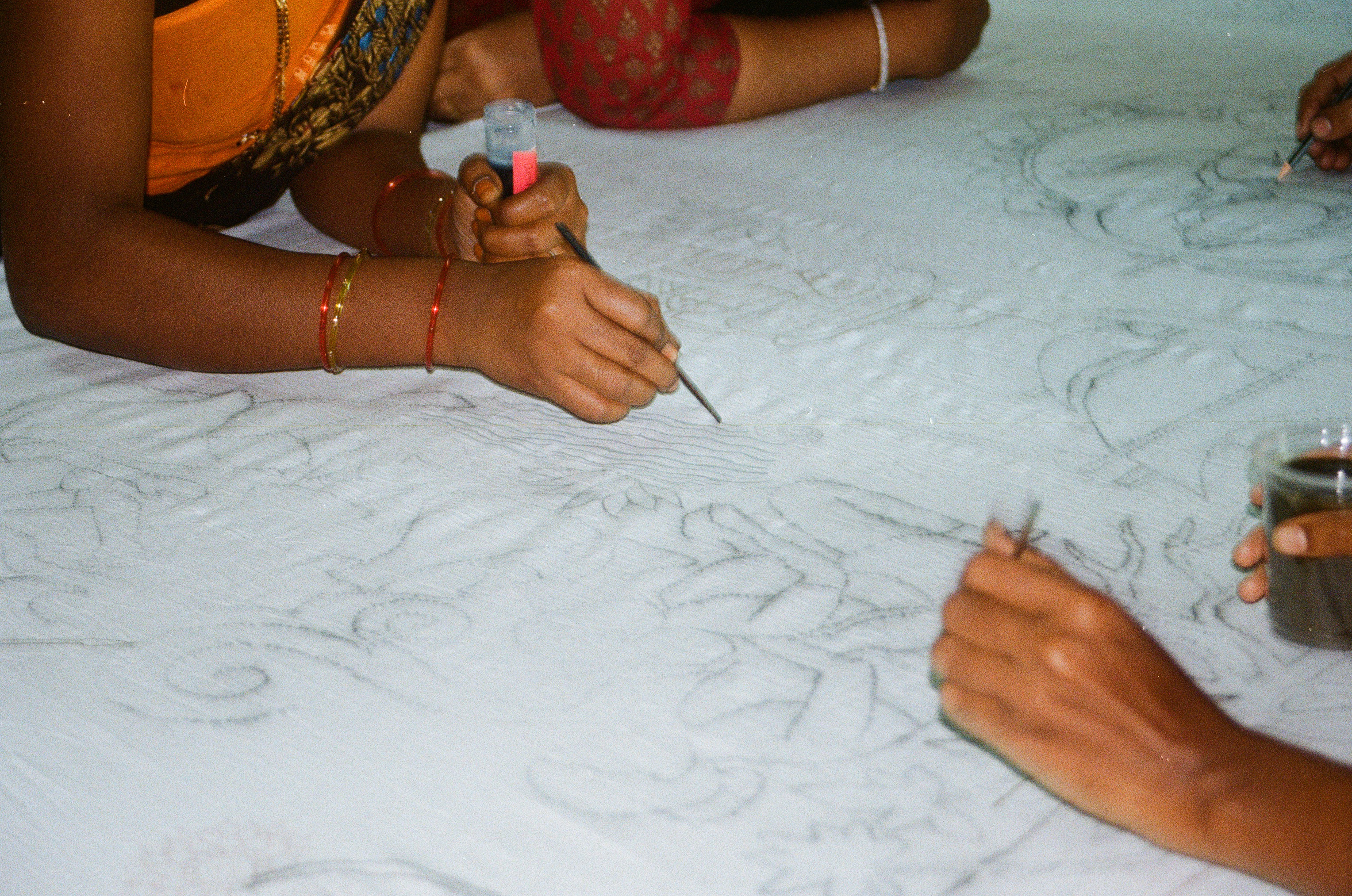 Artisans drawing outlines on cotton with a kalam