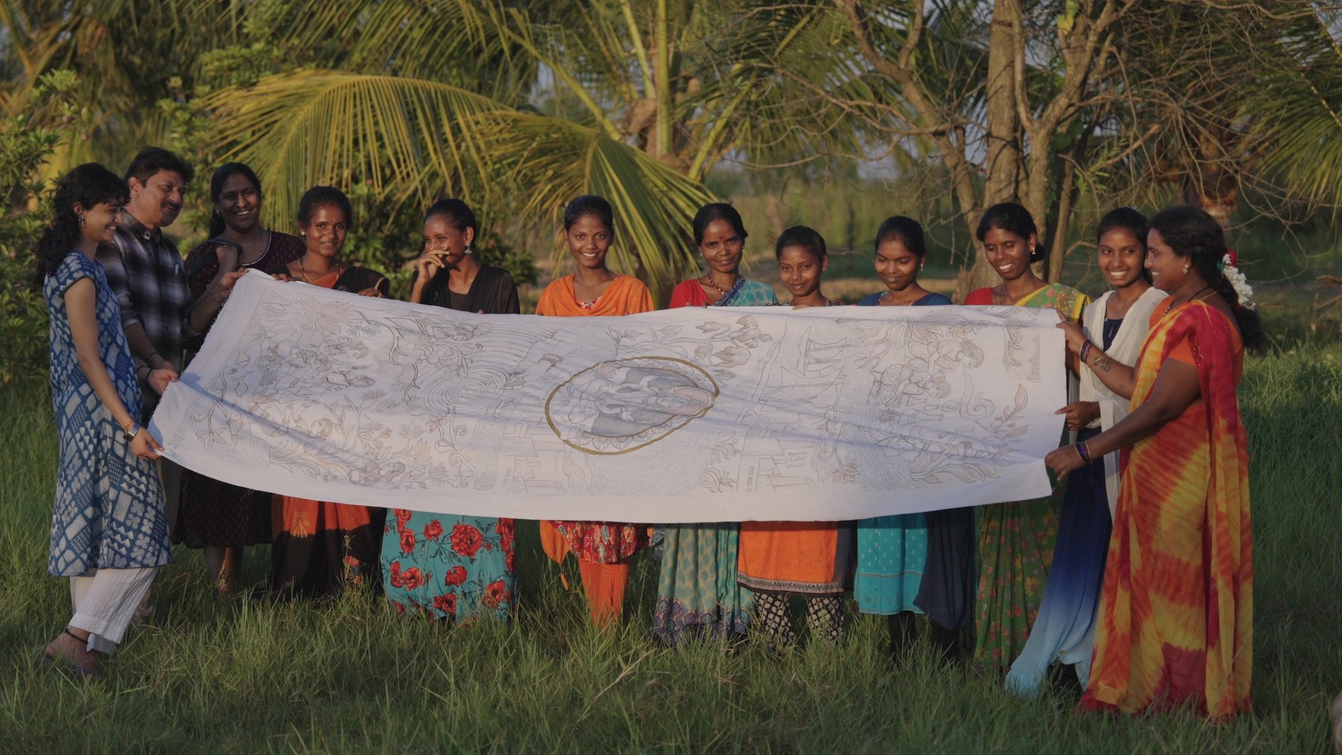 Artisans holding up a length of drawn kalamkari cloth in a field at golden hour